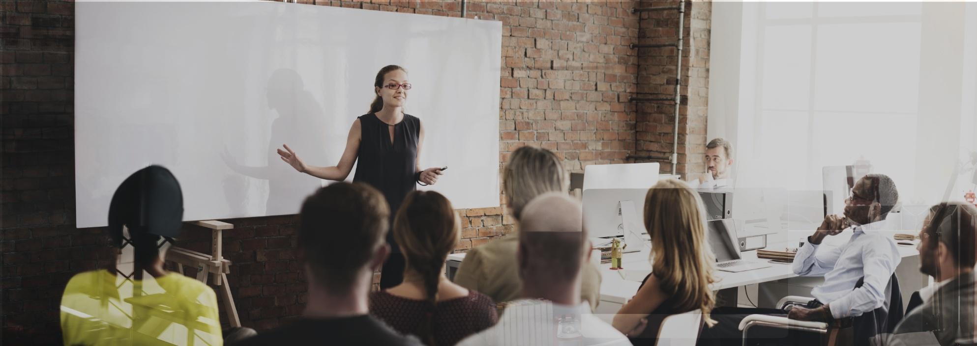 Erwachsenenbildung - Kursleiterin referiert vor einem Smartboard, die Kursgruppe hört aufmerksam zu