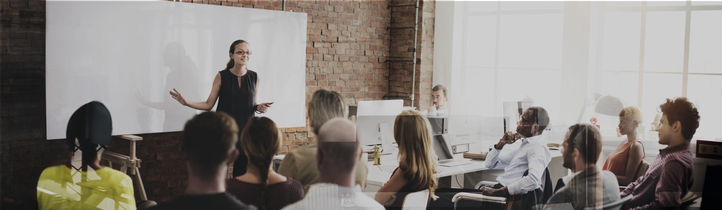 Erwachsenenbildung - Kursleiterin referiert vor einem Smartboard, die Kursgruppe hört aufmerksam zu