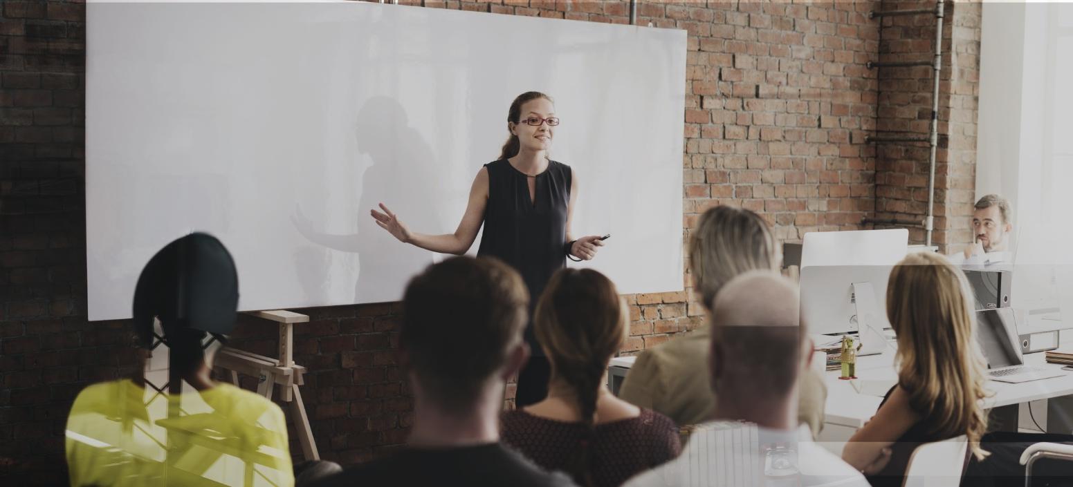 Erwachsenenbildung - Kursleiterin referiert vor einem Smartboard, die Kursgruppe hört aufmerksam zu