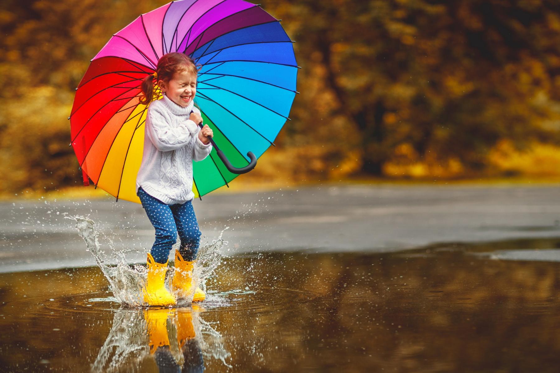 Evgeny_Atamanenko_667327687_Mädchen_springt_im_regen_regenbogenfarbenen_Regenschirm_Herbst