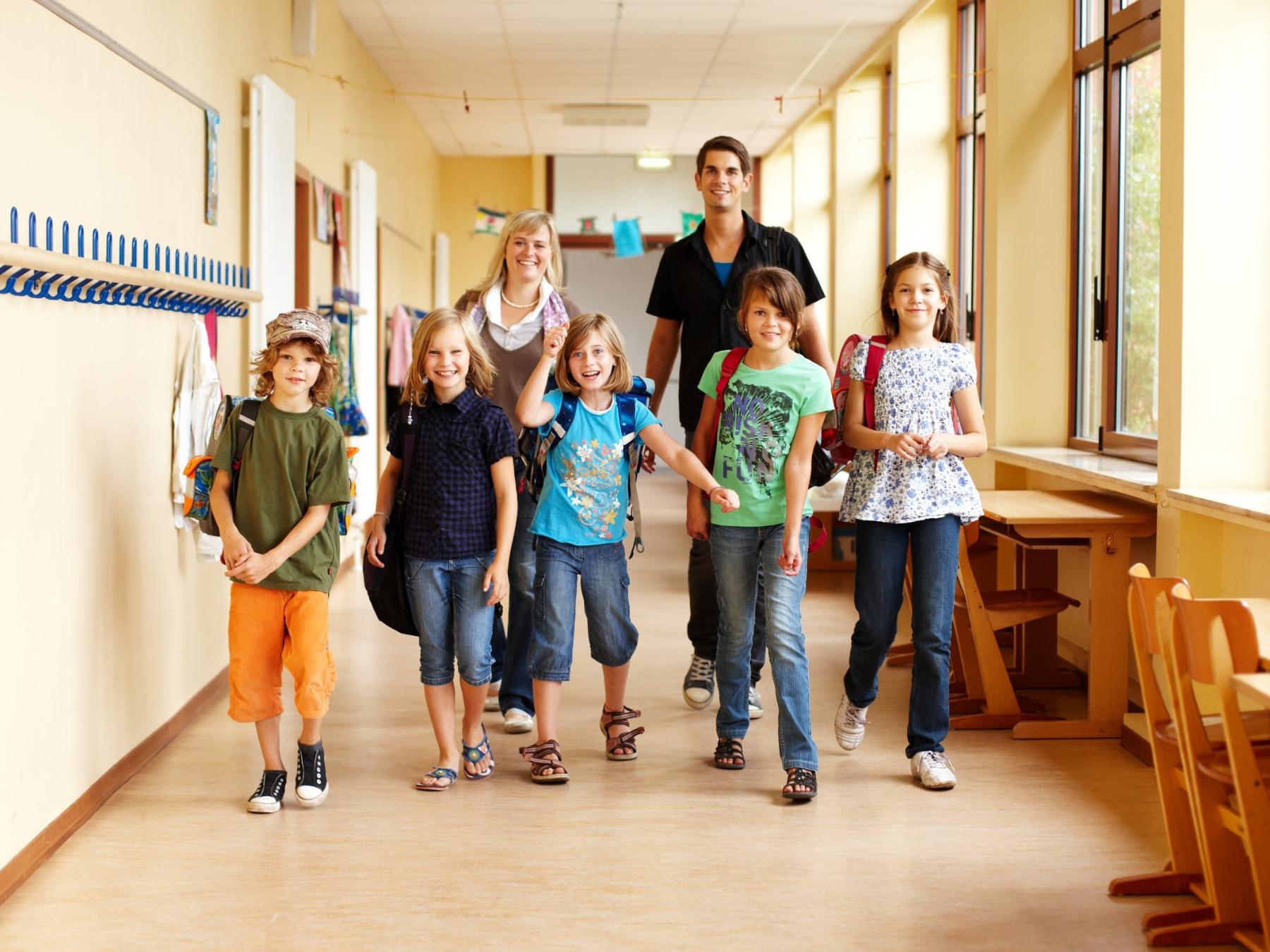 Fünf Schulkinder mit einem Betreuer und einer Betreuerin auf einem Schulflur