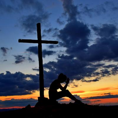 Frau sitzt nachdenklich vor einem Kreuz