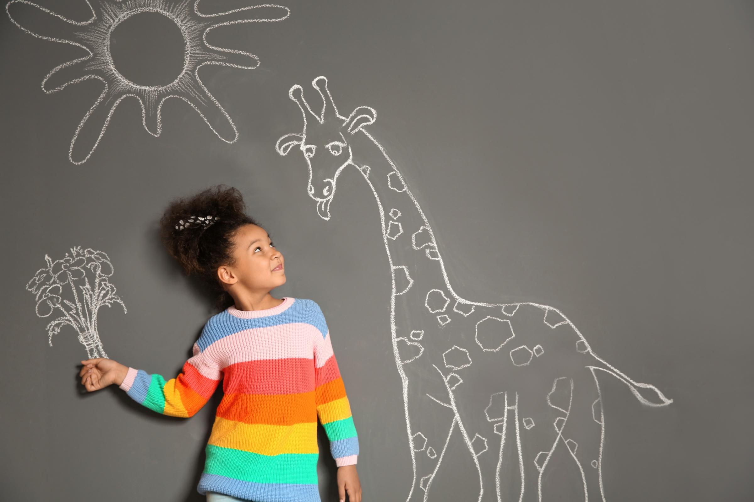 Ein Kind steht vor einer Tafel mit Giraffe und Sonne