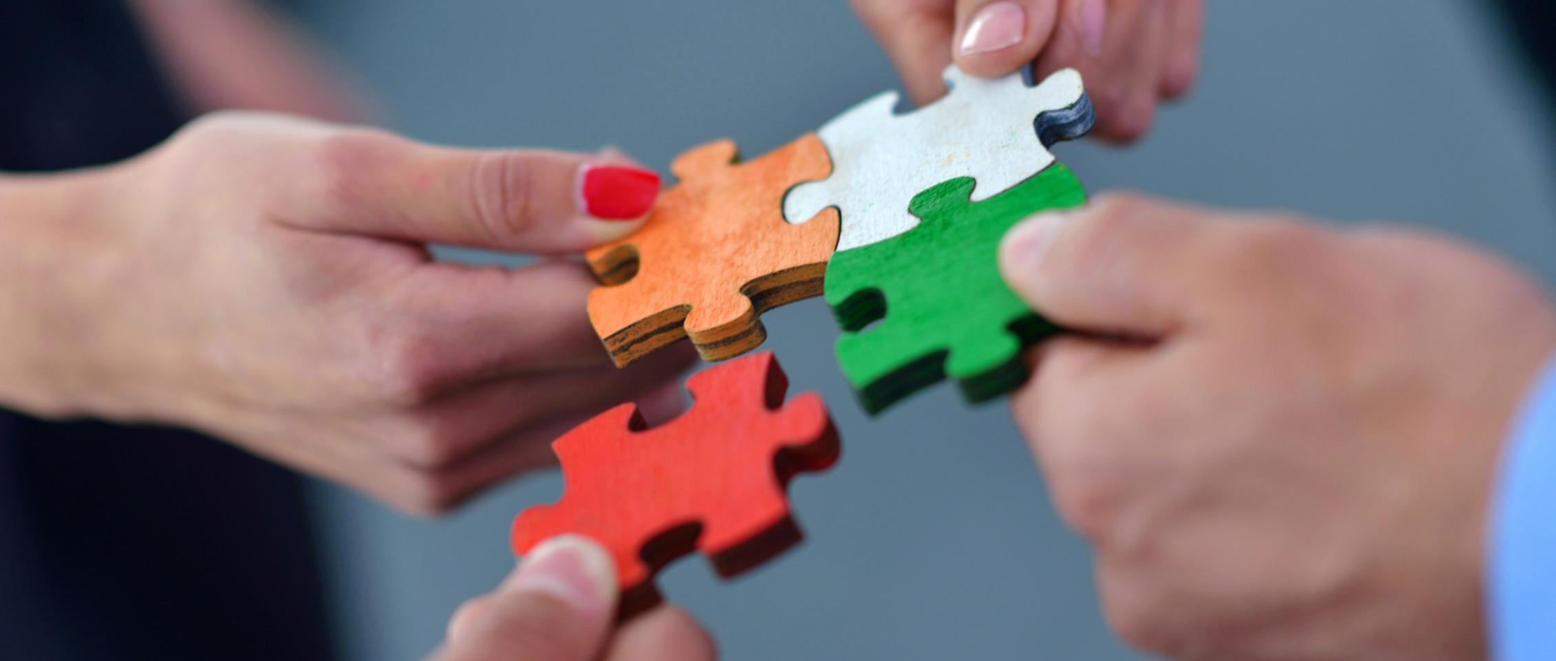Hände setzen bunte Puzzleteile zusammen.