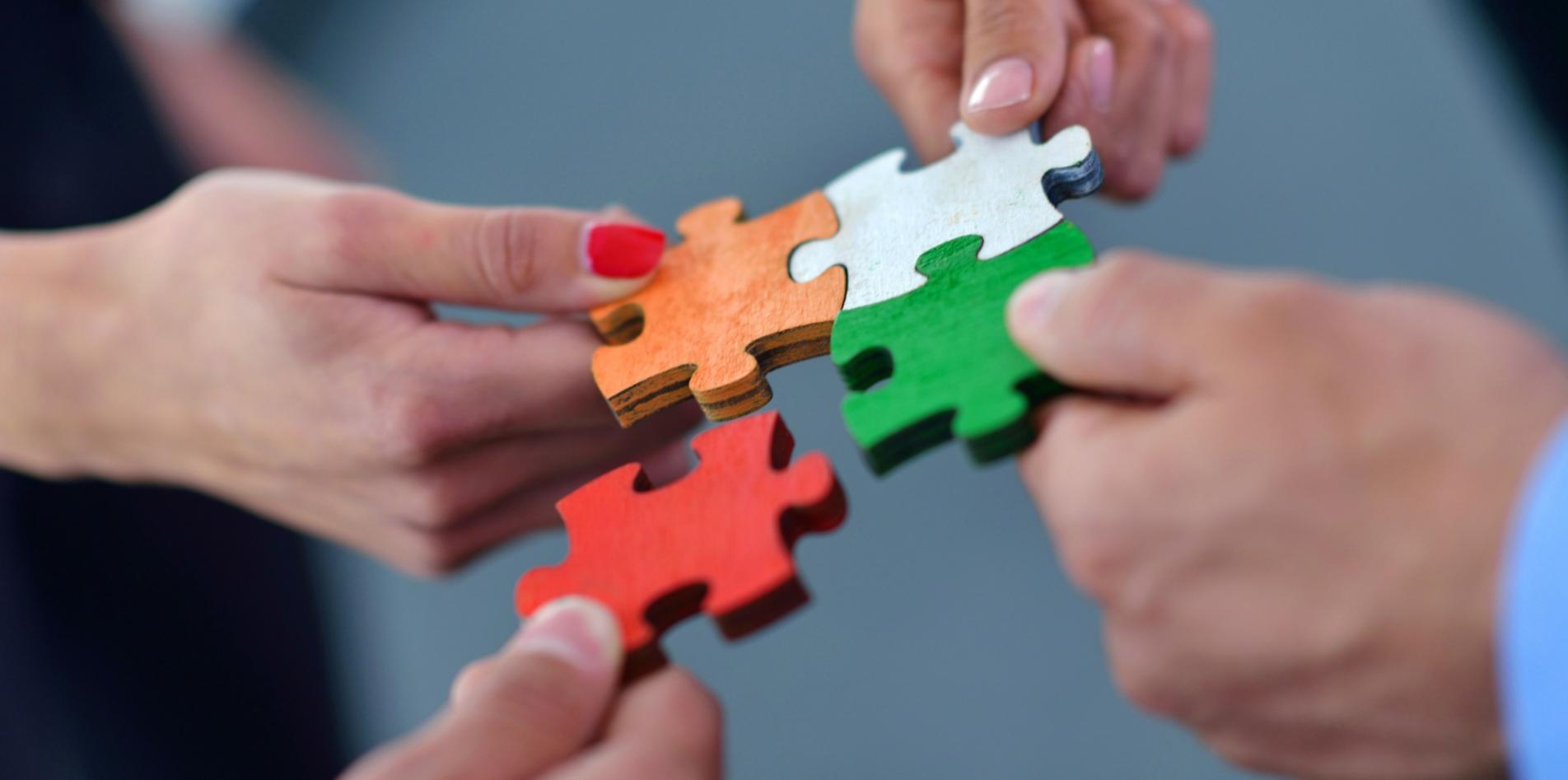 Hände setzen bunte Puzzleteile zusammen.