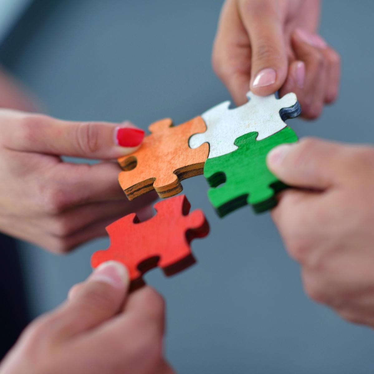 Hände setzen bunte Puzzleteile zusammen.
