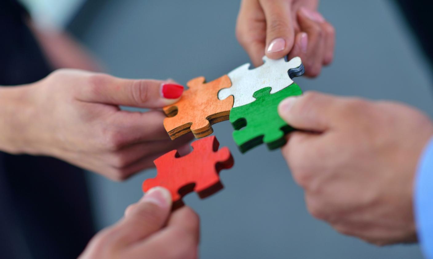 Hände setzen bunte Puzzleteile zusammen.