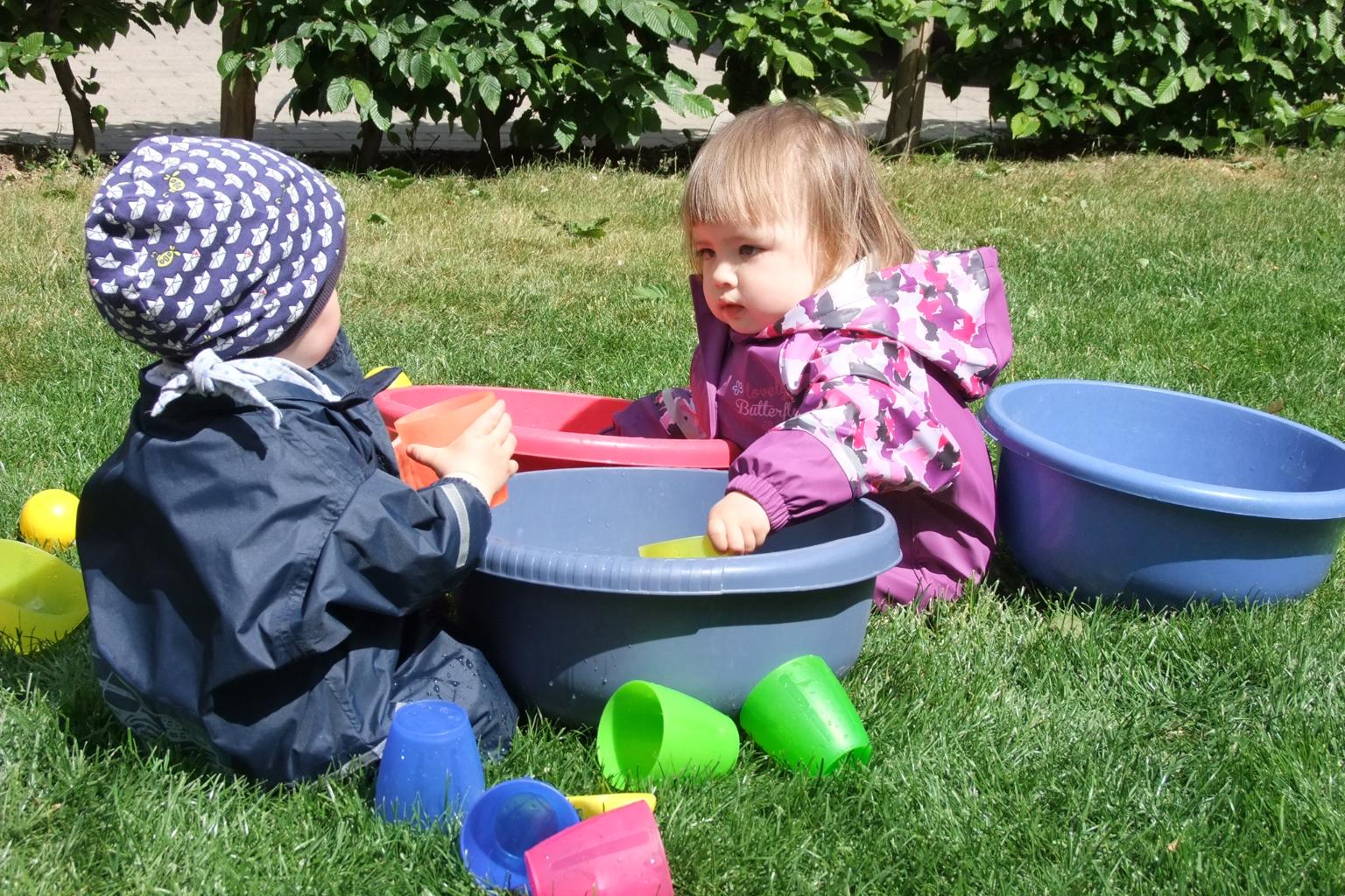Zwei Kleinkinder mit Plastikschüssel auf dem Rasen