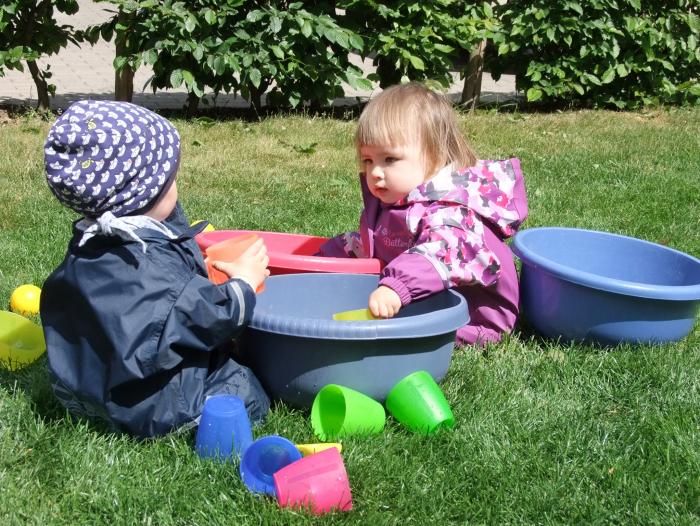 Zwei Kleinkinder mit Plastikschüssel auf dem Rasen