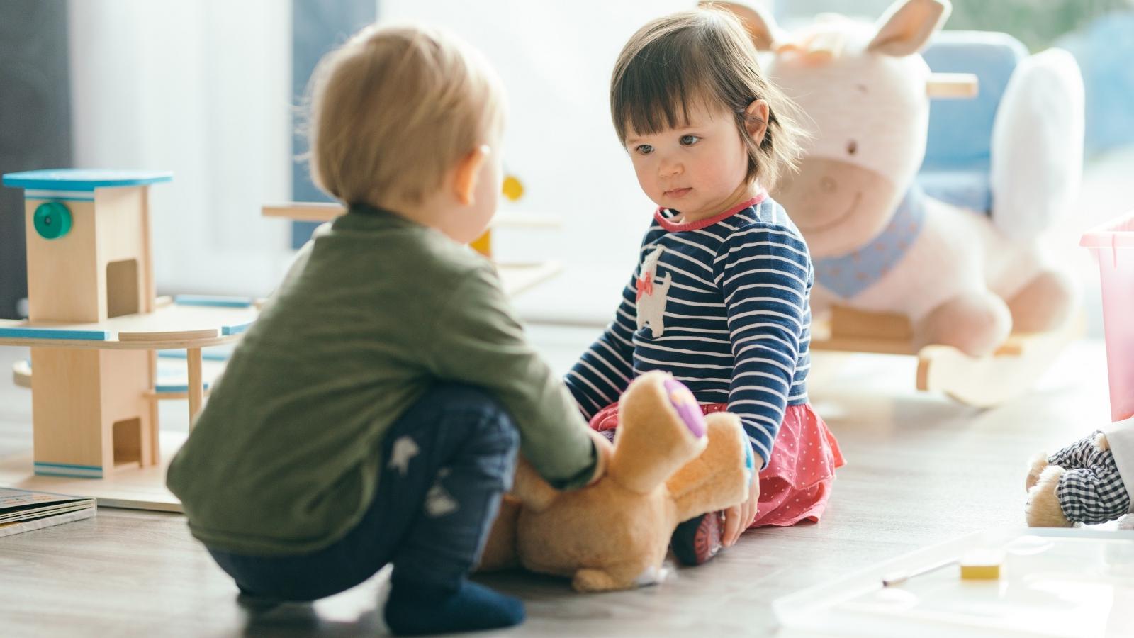 Zwei Kinder spielen zusammen mit einem Teddybären.